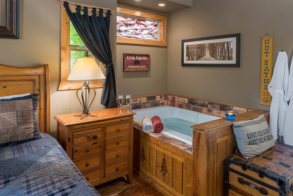 A cozy bedroom corner featuring a large in-room Jacuzzi tub with a stone-tile border, positioned beneath a decorative stained-glass window.