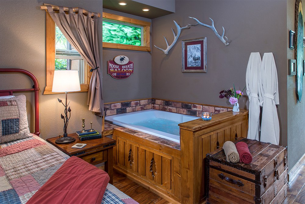 Bedroom corner featuring a built-in wooden Jacuzzi tub with stone tile trim, set against a gray wall decorated with white antlers and a small framed picture.