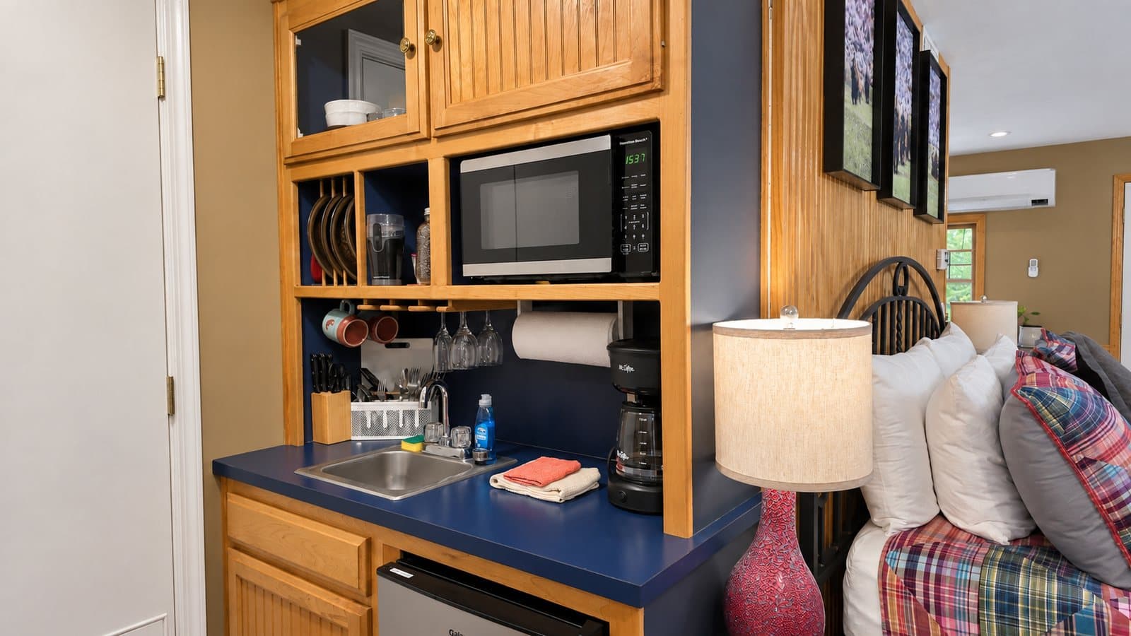 A small kitchen area featuring a microwave, sink, and coffee maker, adjacent to a cozy sleeping space.