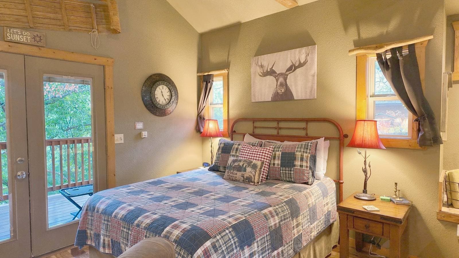 Cozy bedroom with a plaid bedspread, wooden accents, and large windows overlooking a balcony.