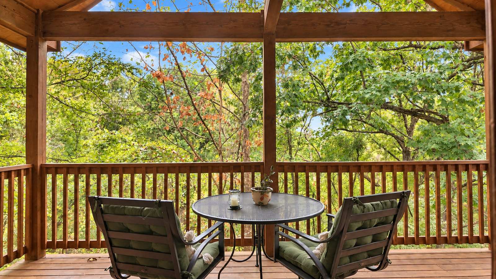 A cozy deck with two chairs and a table, surrounded by lush green trees.