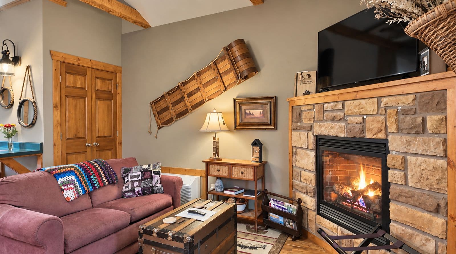 Cozy living room featuring a stone fireplace, a pink sofa, and rustic wood accents.