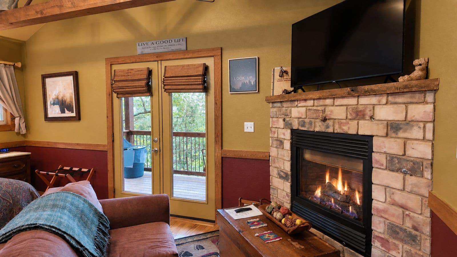 Cozy living room featuring a stone fireplace, TV, and double doors leading to a deck.