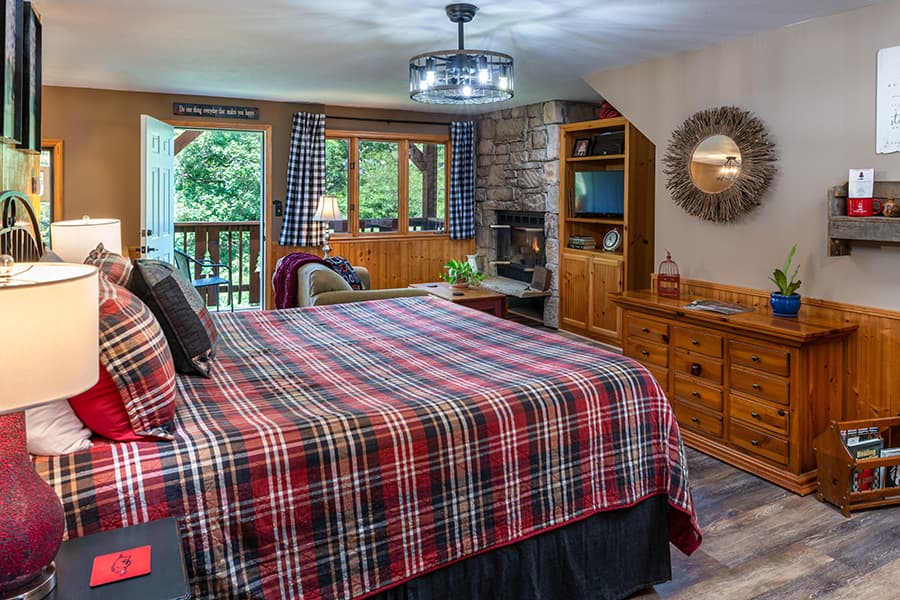 Cozy bedroom featuring a plaid bedspread, wooden furniture, and large windows overlooking a natural setting.