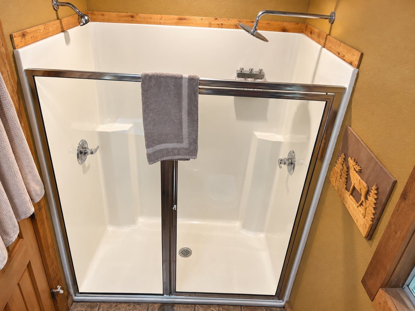 A modern corner shower with glass doors, a towel hanging, and wooden accents.
