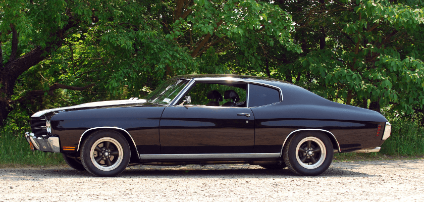 A classic black muscle car parked on a gravel road with lush green trees in the background. A classic black muscle car parked on a gravel road with lush green trees in the background.