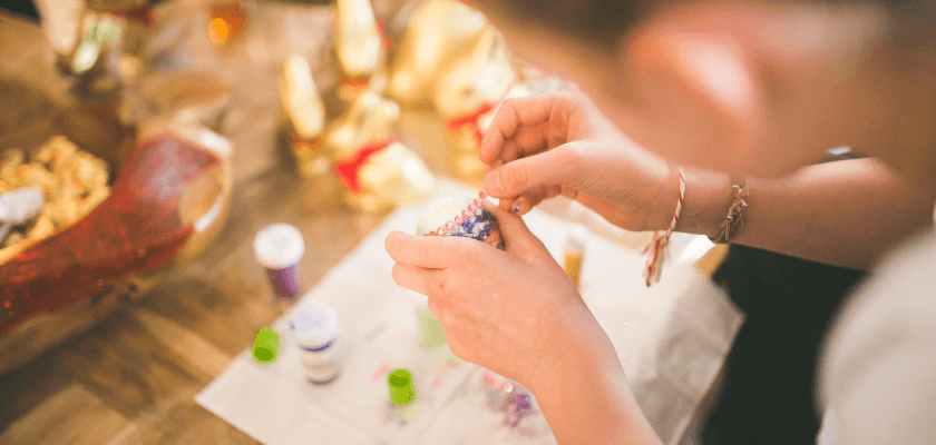 A person decorates a small object with colorful beads and paint. A person decorates a small object with colorful beads and paint.