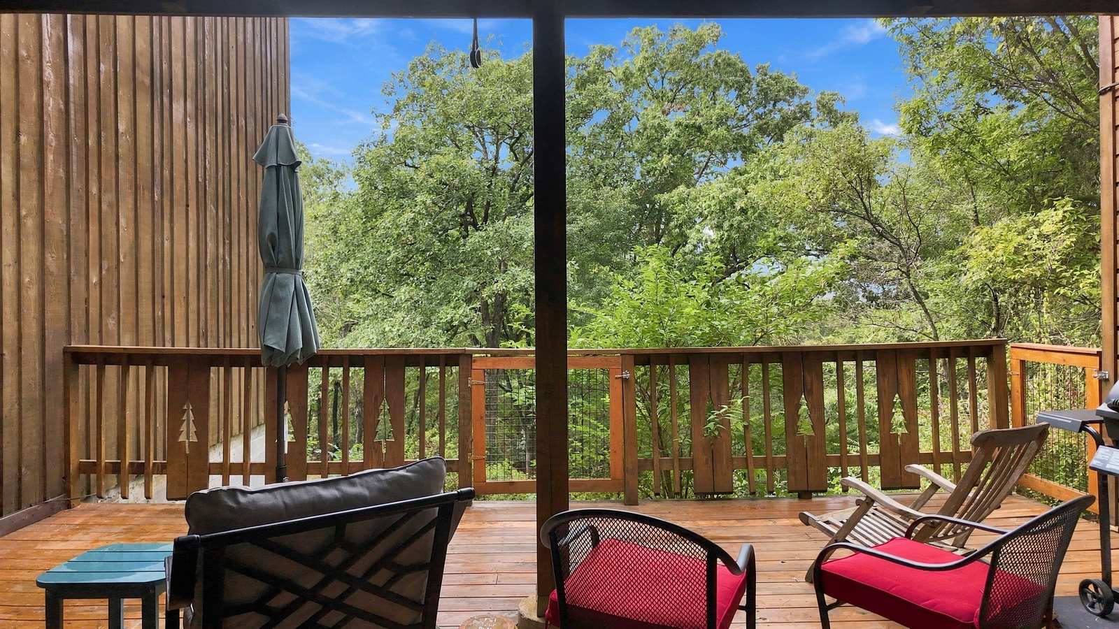 A wooden deck with two chairs overlooks a vibrant green landscape under a clear blue sky.