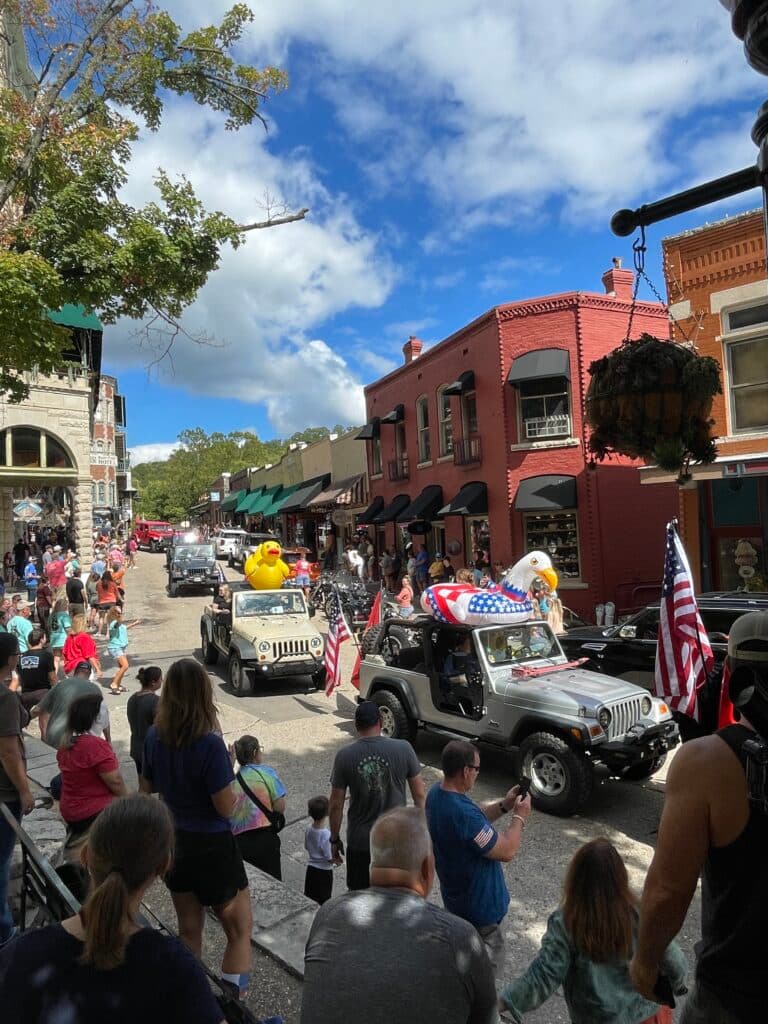 A festive parade featuring decorated vehicles and a crowd of onlookers on a vibrant street.