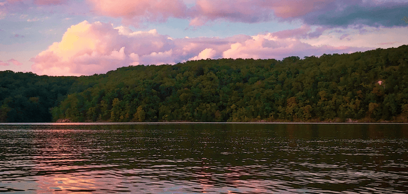 A tranquil river scene reflecting a green forest and colorful clouds at sunset. A tranquil river scene reflecting a green forest and colorful clouds at sunset.