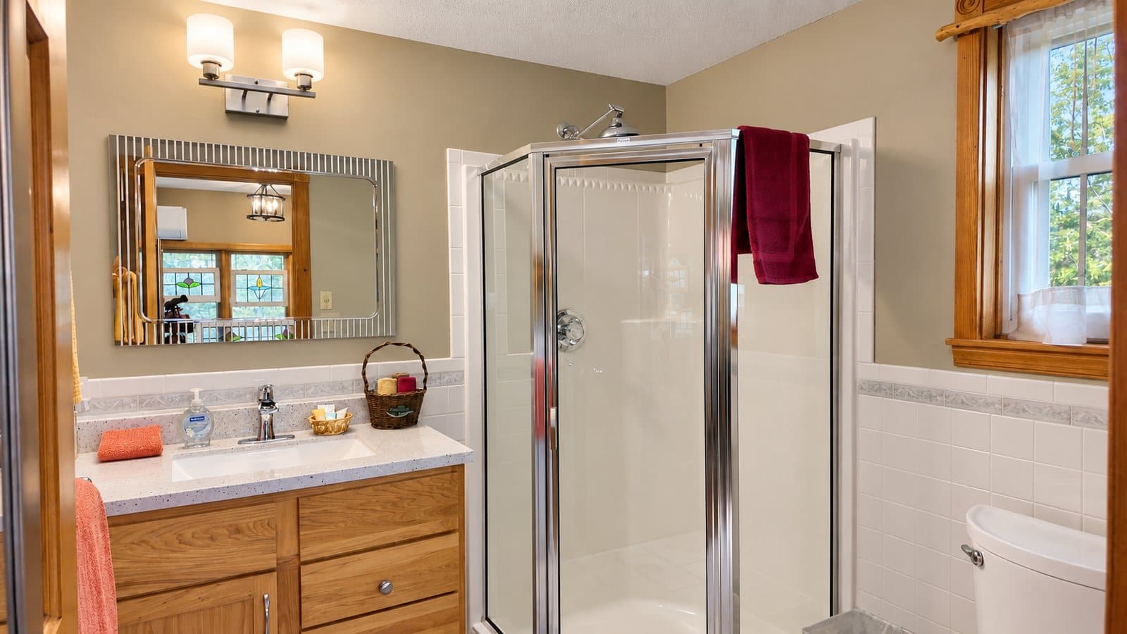 A modern bathroom featuring a glass shower, wooden cabinetry, and natural light from a window.