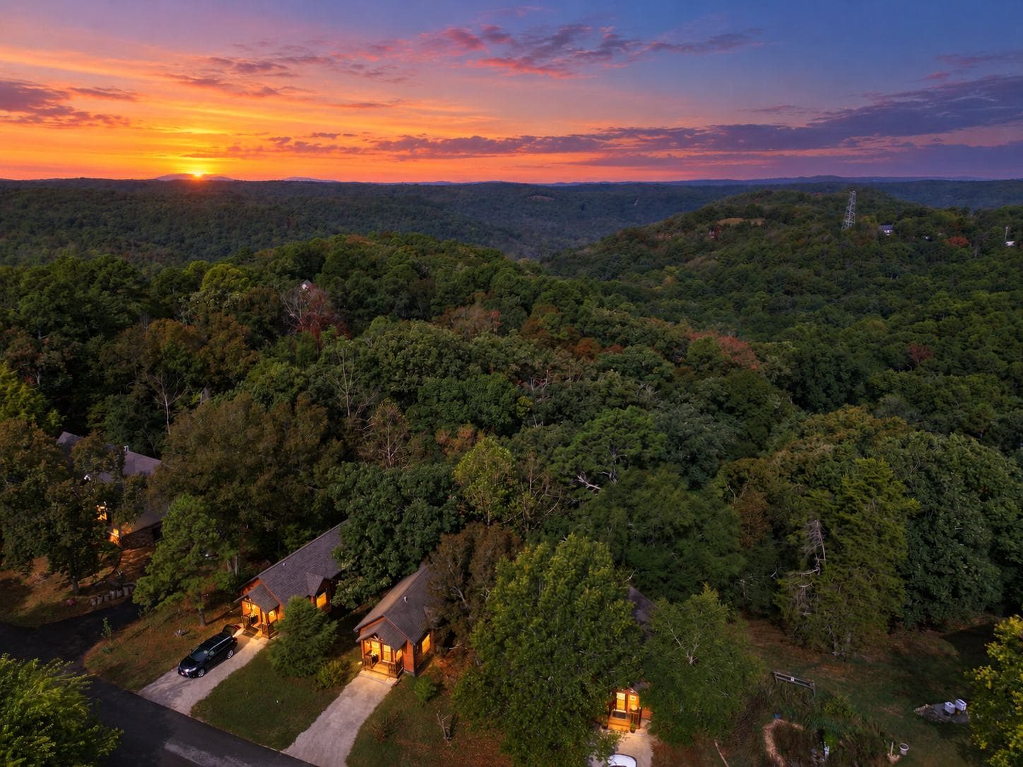 Aerial view of rustic cabins surrounded by lush greenery at sunset.