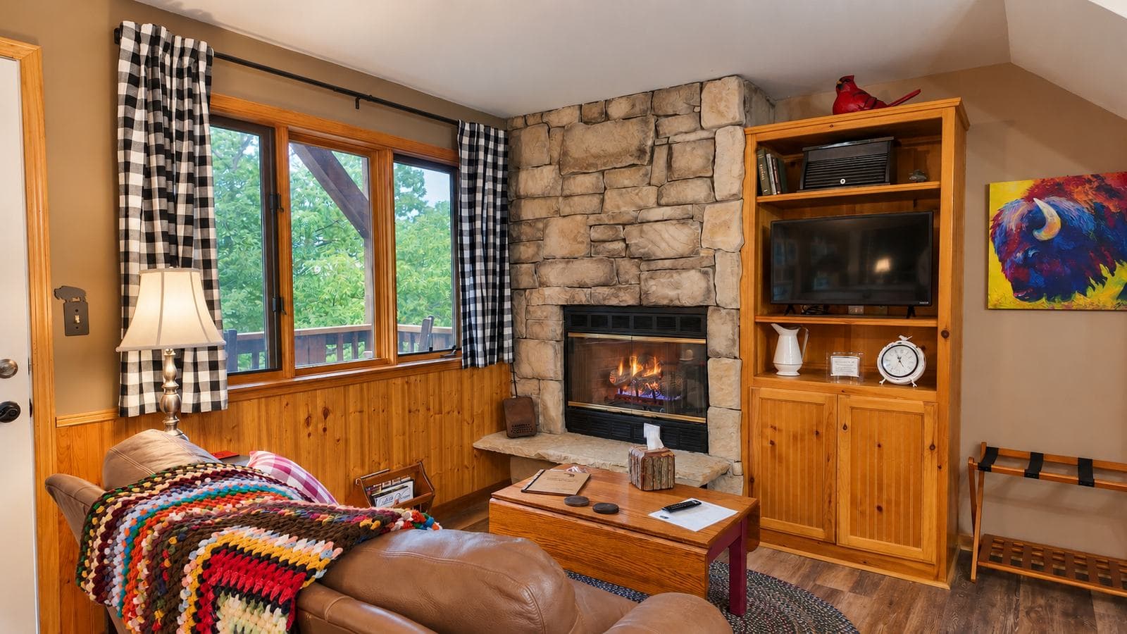 Cozy living room with a stone fireplace, wooden accents, and large windows.