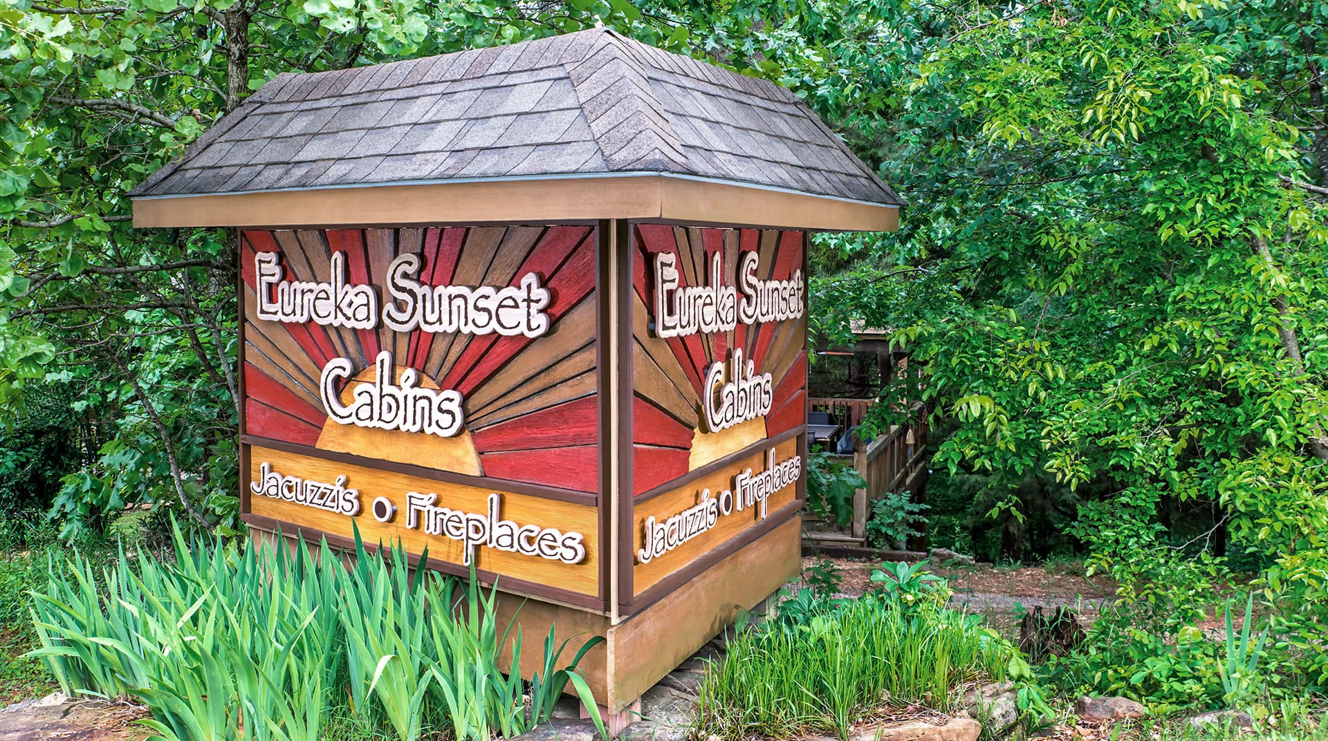 A wooden sign for Eureka Sunset Cabins, surrounded by greenery, highlighting amenities like jacuzzis and fireplaces.