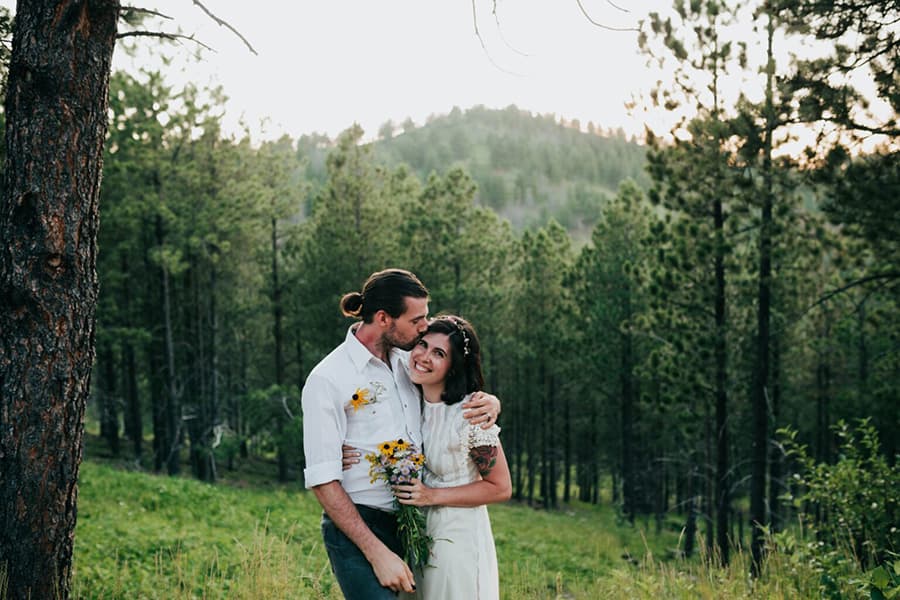 A couple embraces in a lush forest while holding a bouquet of wildflowers.