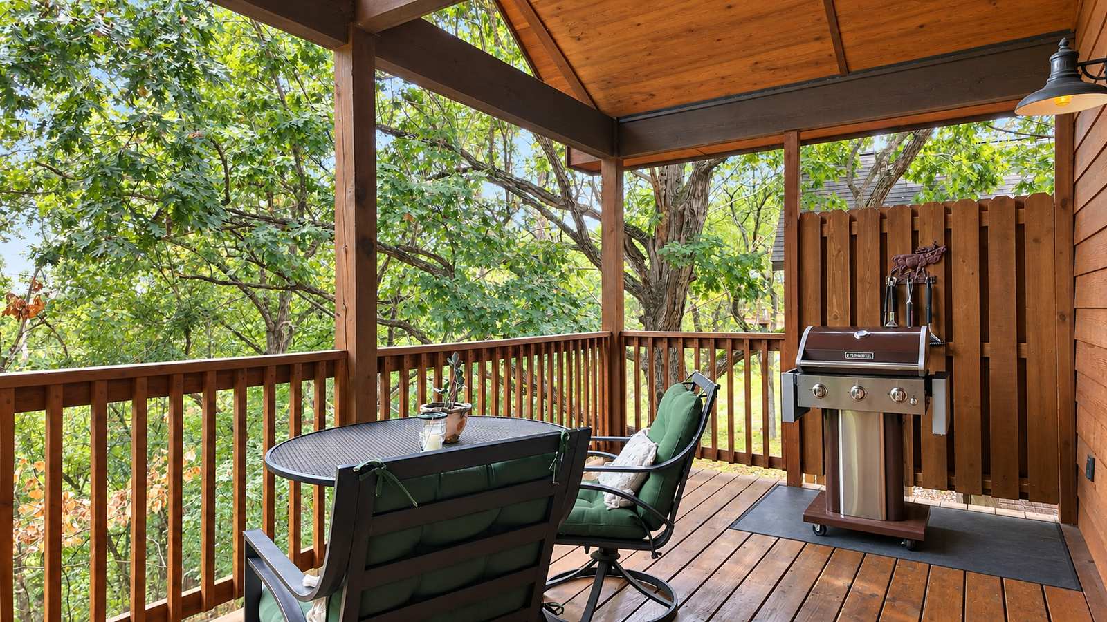 A cozy balcony with a grilling station, table, and chairs surrounded by greenery.