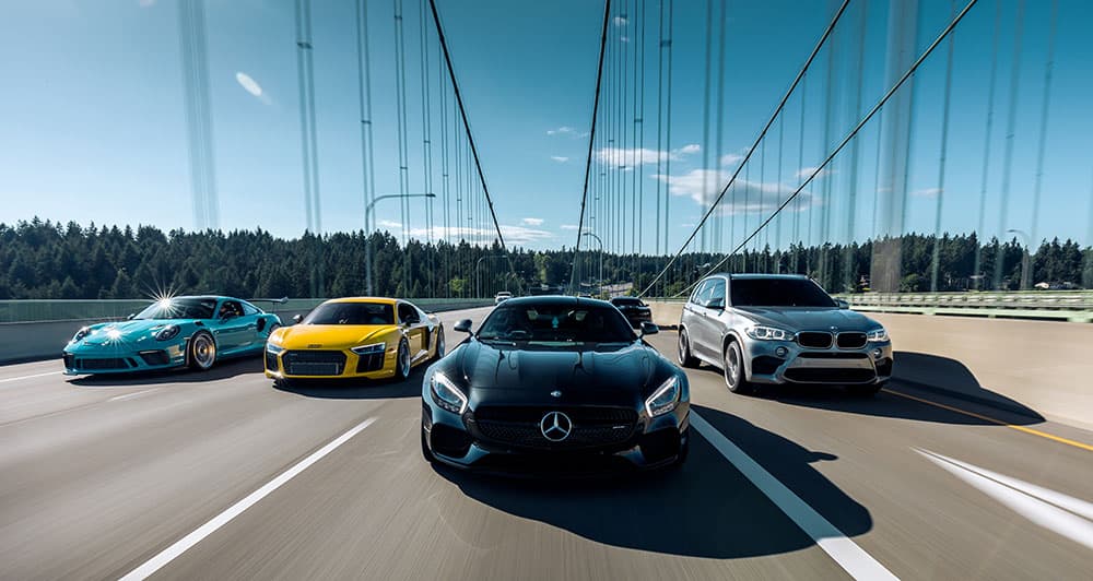 A lineup of luxury sports cars driving on a bridge under a clear blue sky. A lineup of luxury sports cars driving on a bridge under a clear blue sky.