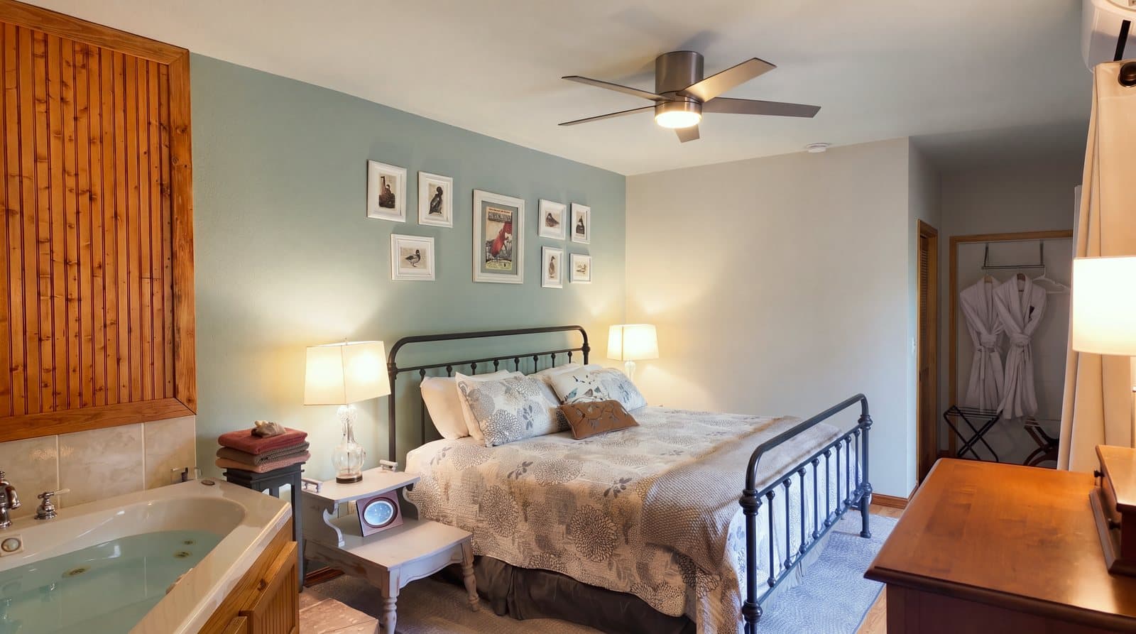 Cozy bedroom featuring a double bed, bedside tables, framed art, and a jetted tub.