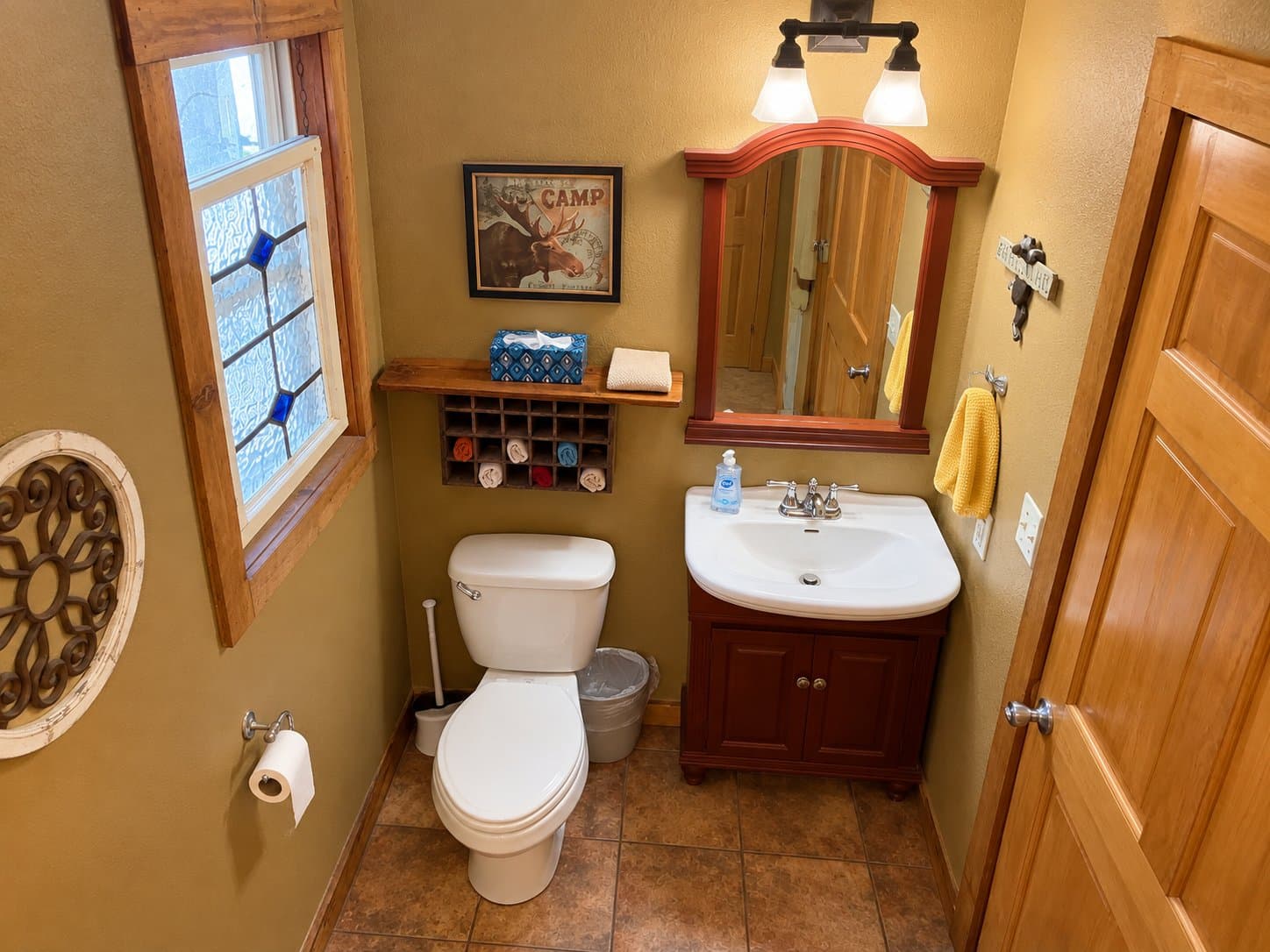 A compact bathroom featuring a toilet, sink, and mirror, with natural light and rustic decor.