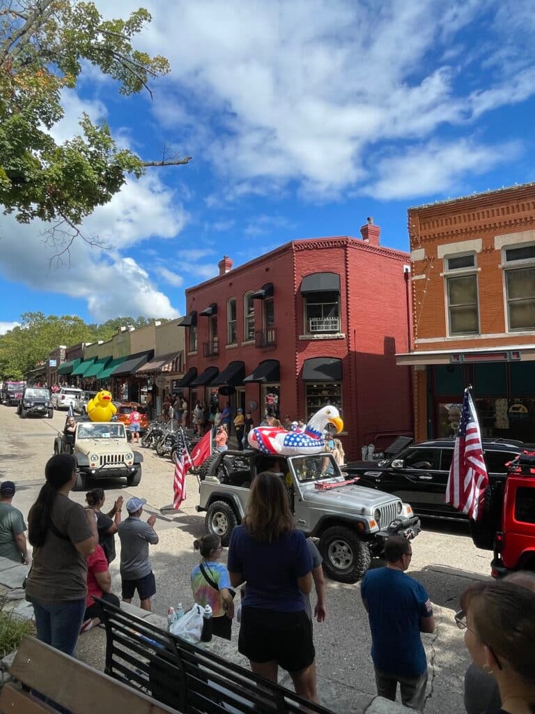A parade featuring decorated jeeps and onlookers in a lively downtown setting under a cloudy sky.