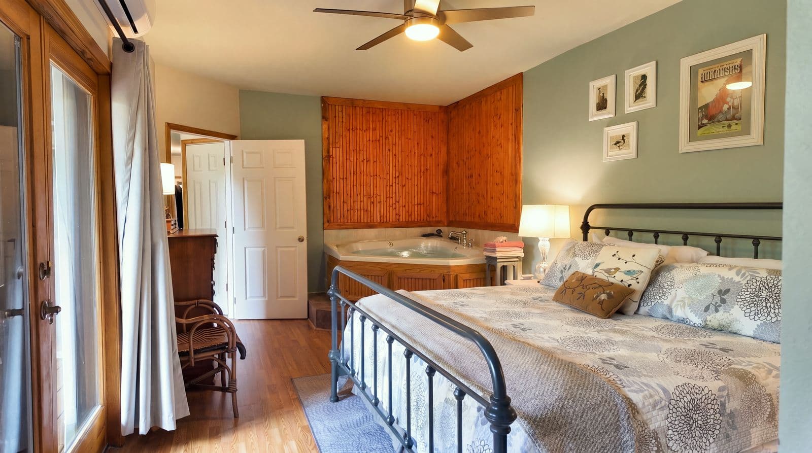 Cozy bedroom featuring a metal-framed bed, a jetted tub, and natural light from large windows.