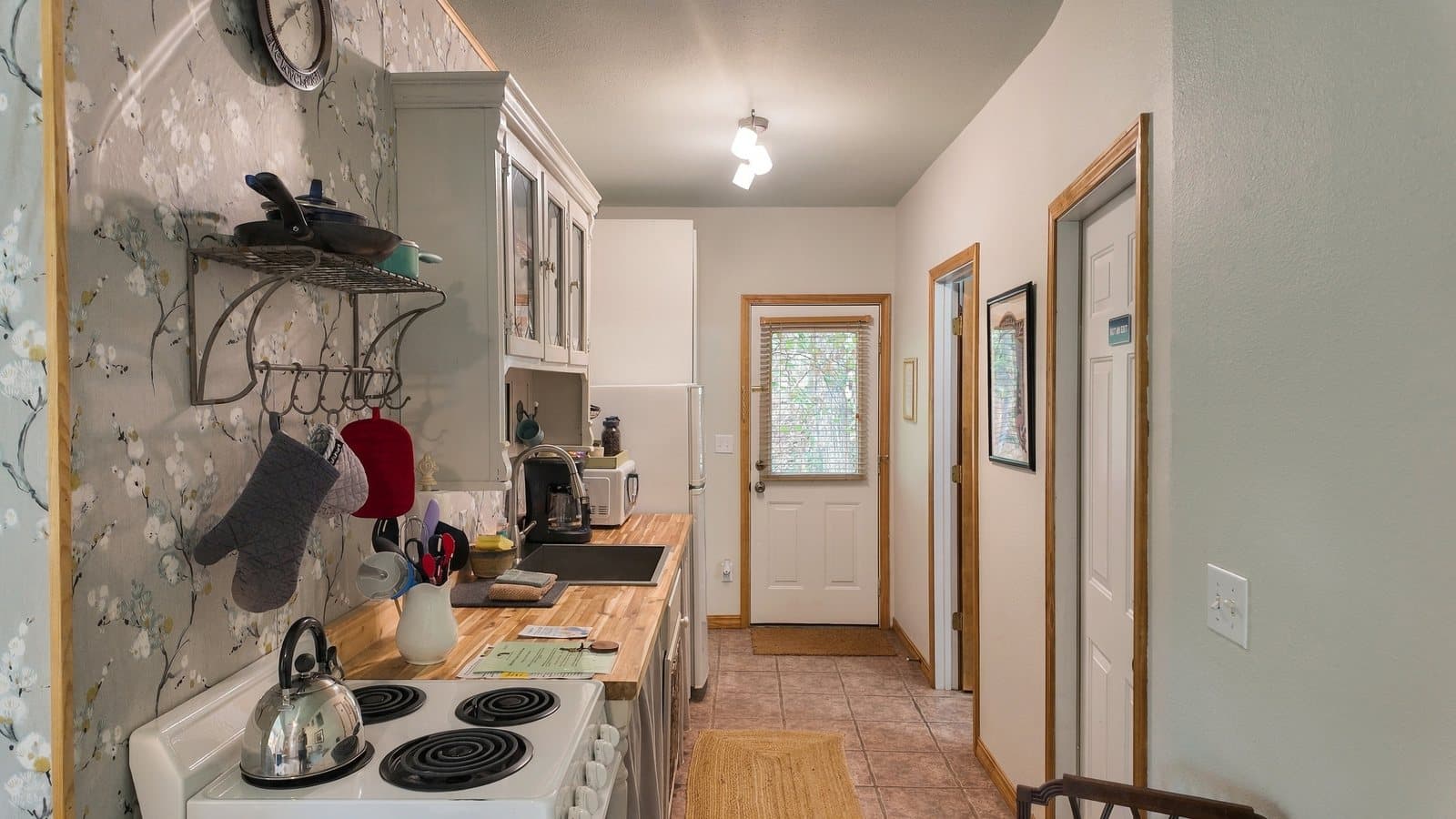 A narrow kitchen with white cabinetry, a stove, and a door leading outside.