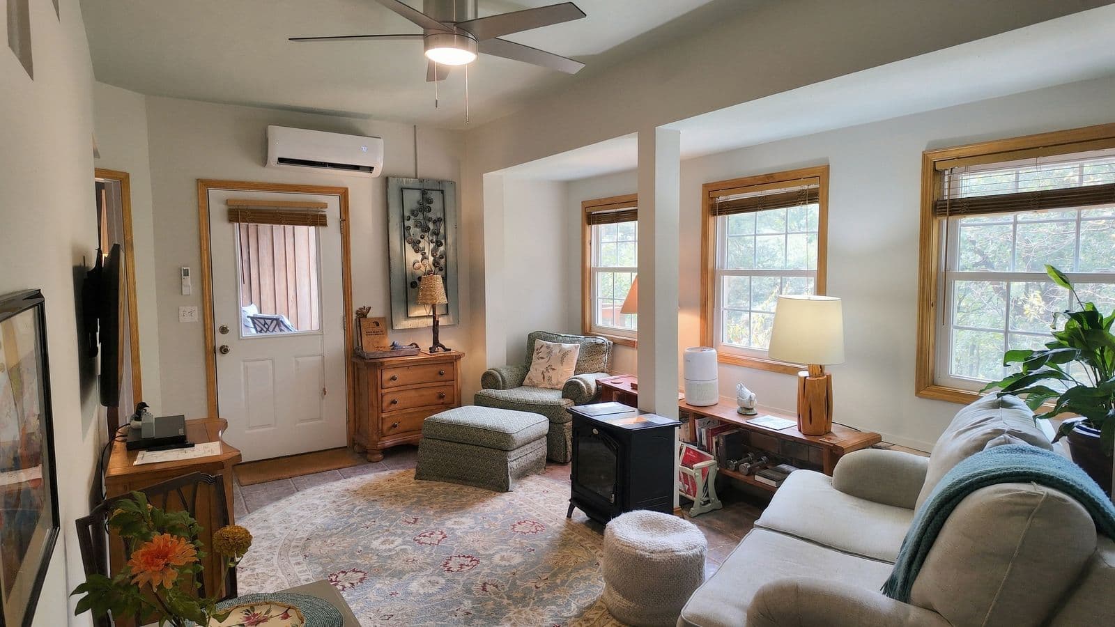 Cozy living room with a ceiling fan, large windows, comfortable seating, and decorative elements.