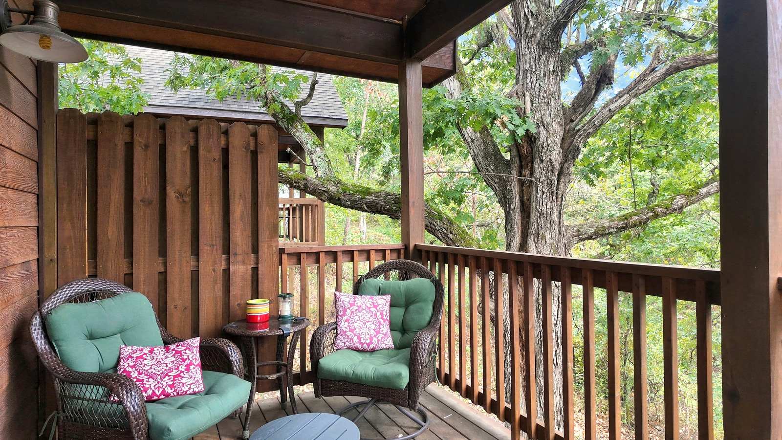 Cozy porch with two green chairs and decorative pillows nestled among trees.