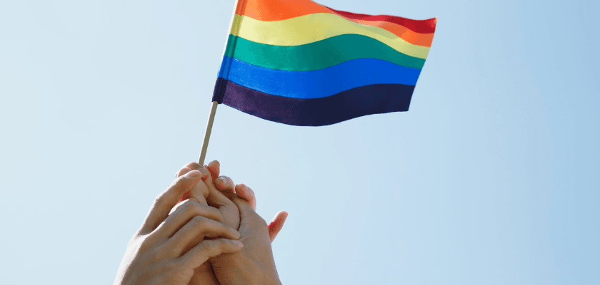 Two hands holding a rainbow flag against a clear sky. Two hands holding a rainbow flag against a clear sky.
