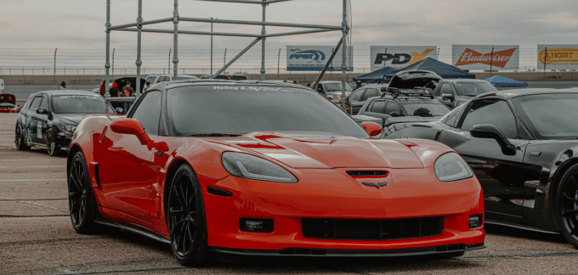 A sleek orange sports car is parked at an event with other vehicles in the background. A sleek orange sports car is parked at an event with other vehicles in the background.
