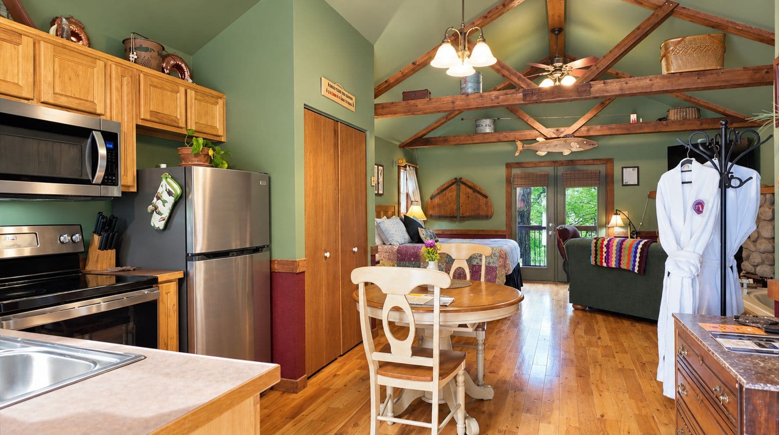 Cozy cabin interior featuring a kitchen, dining area, and living space with wooden beams and green walls.