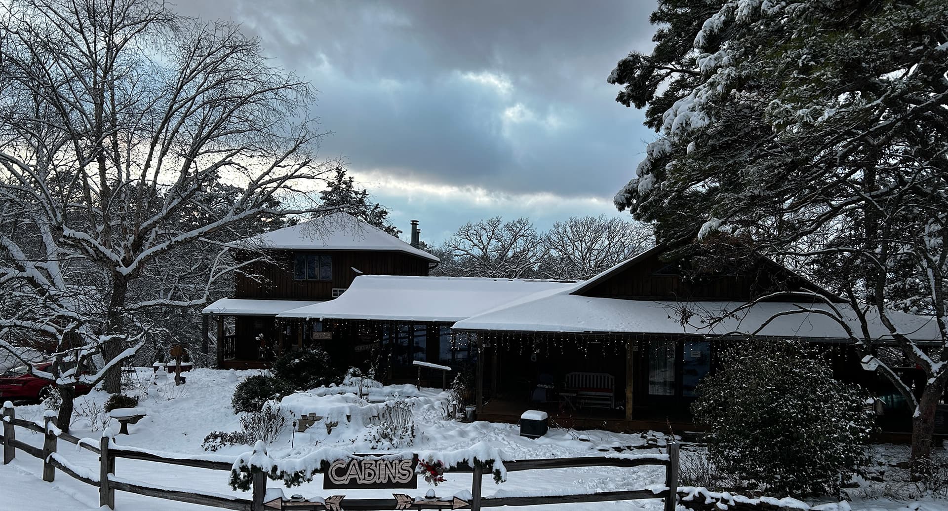 A snow-covered cabin surrounded by trees and cloudy skies.
