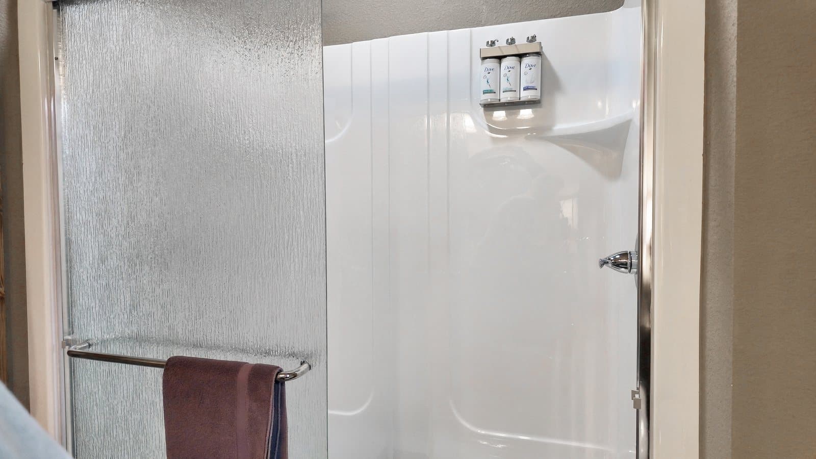 A shower area with a frosted glass door and a towel rack holding a purple towel.