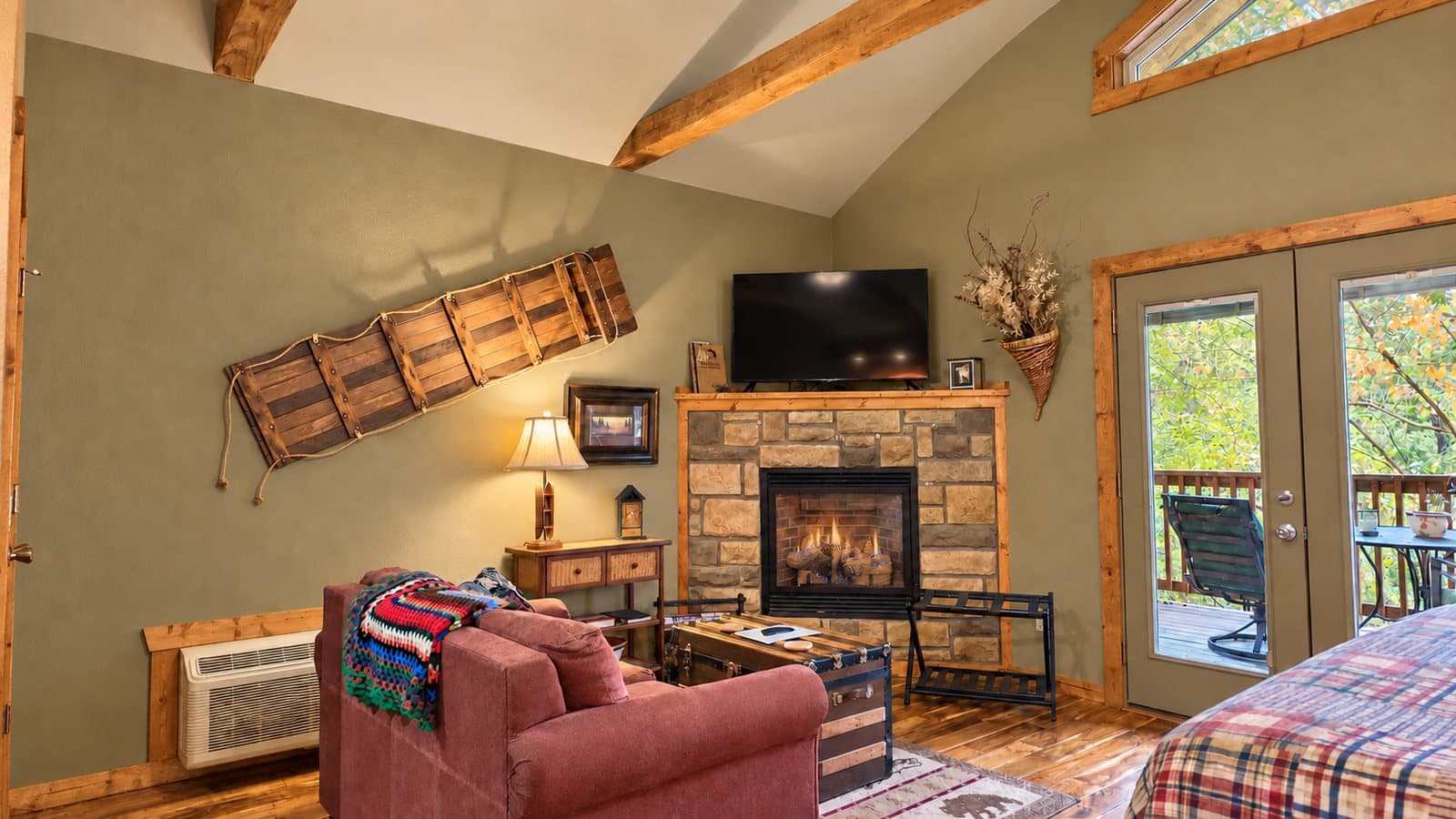 A cozy living room featuring a stone fireplace, wooden beams, and large windows overlooking nature.