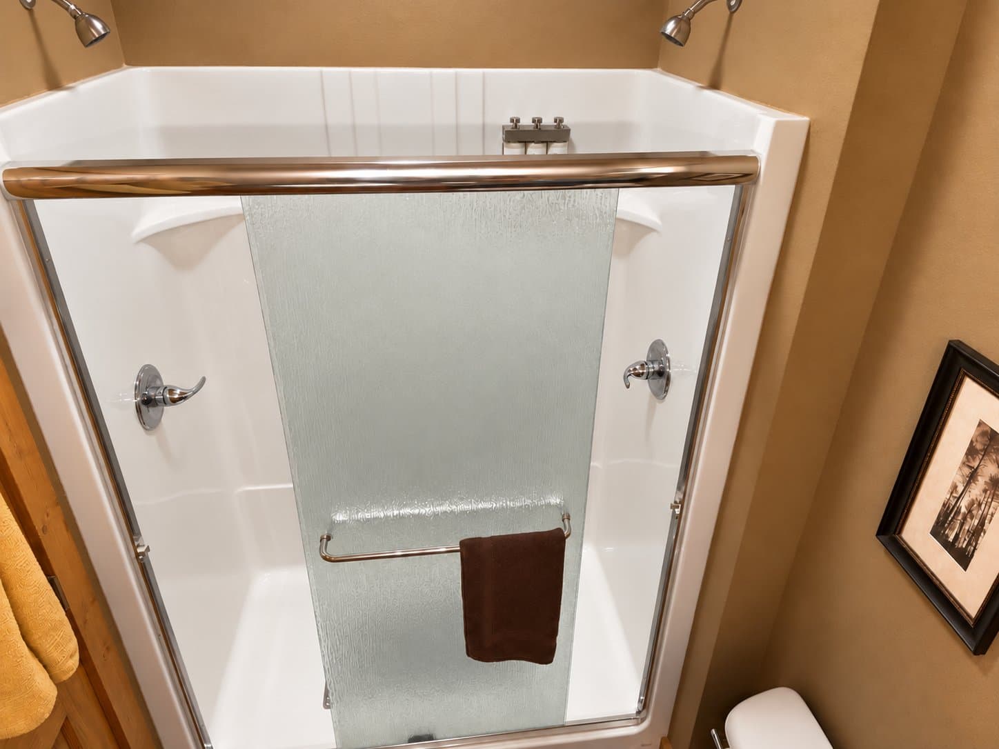 A modern shower stall with a glass door, a brown towel hanging, and beige walls.
