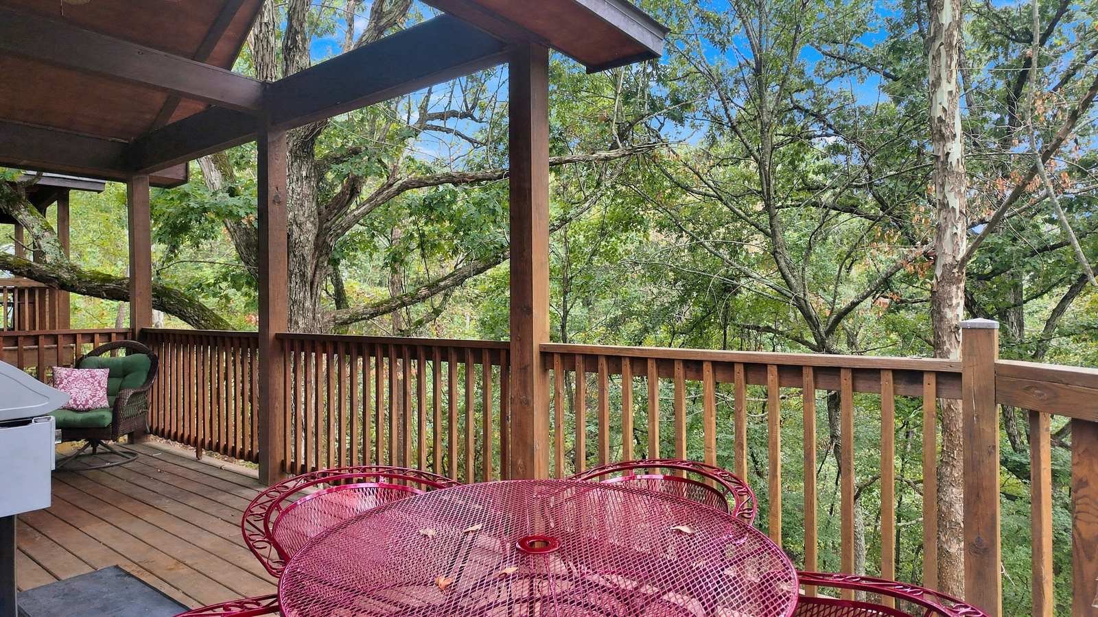 A red metal table and chairs on a wooden deck surrounded by trees.