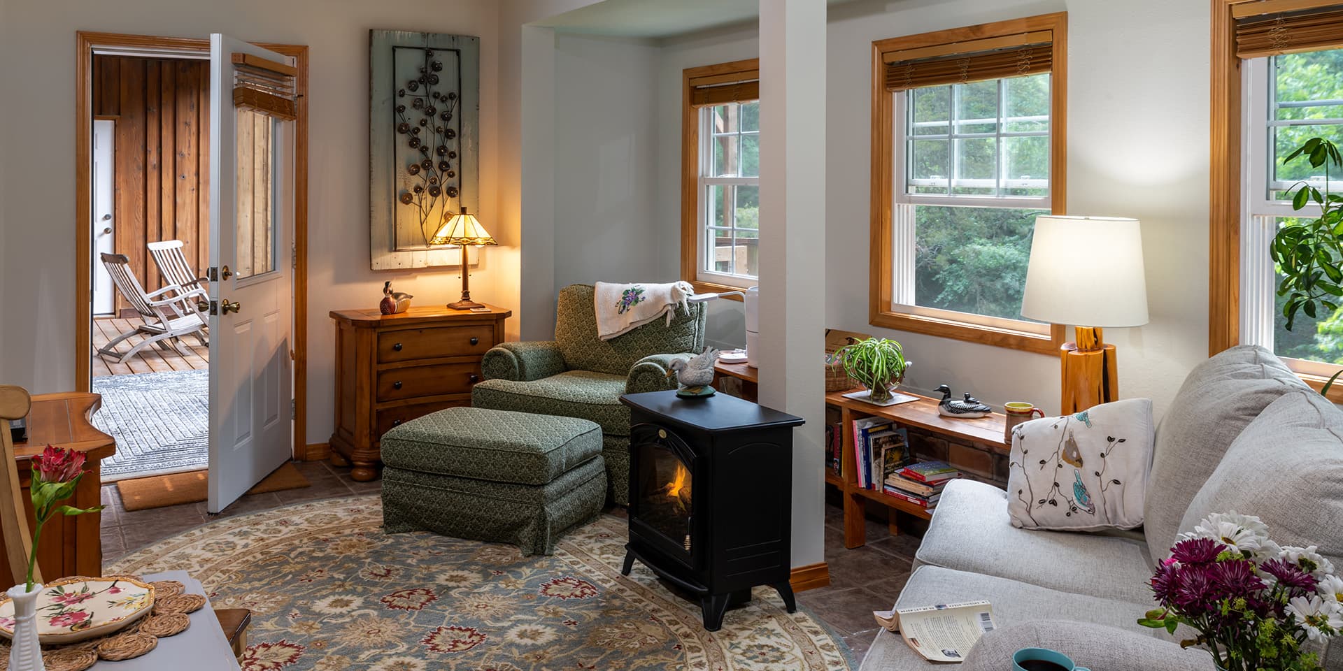 Cozy living room with a green chair, a lamp, and large windows letting in natural light.