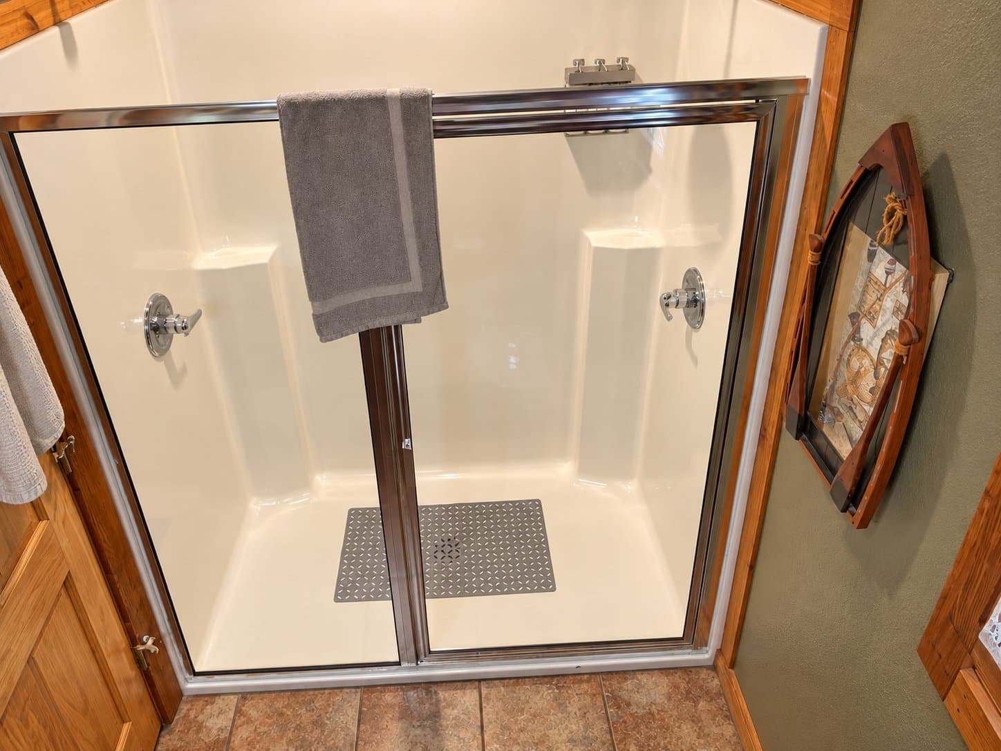 A modern shower enclosure with sliding glass doors and a gray towel hanging on the rail.