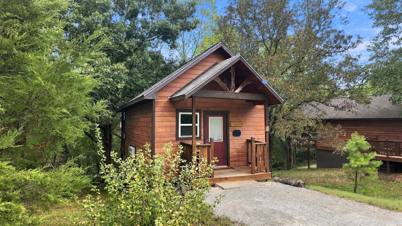 A small wooden cabin surrounded by greenery and featuring a front porch.