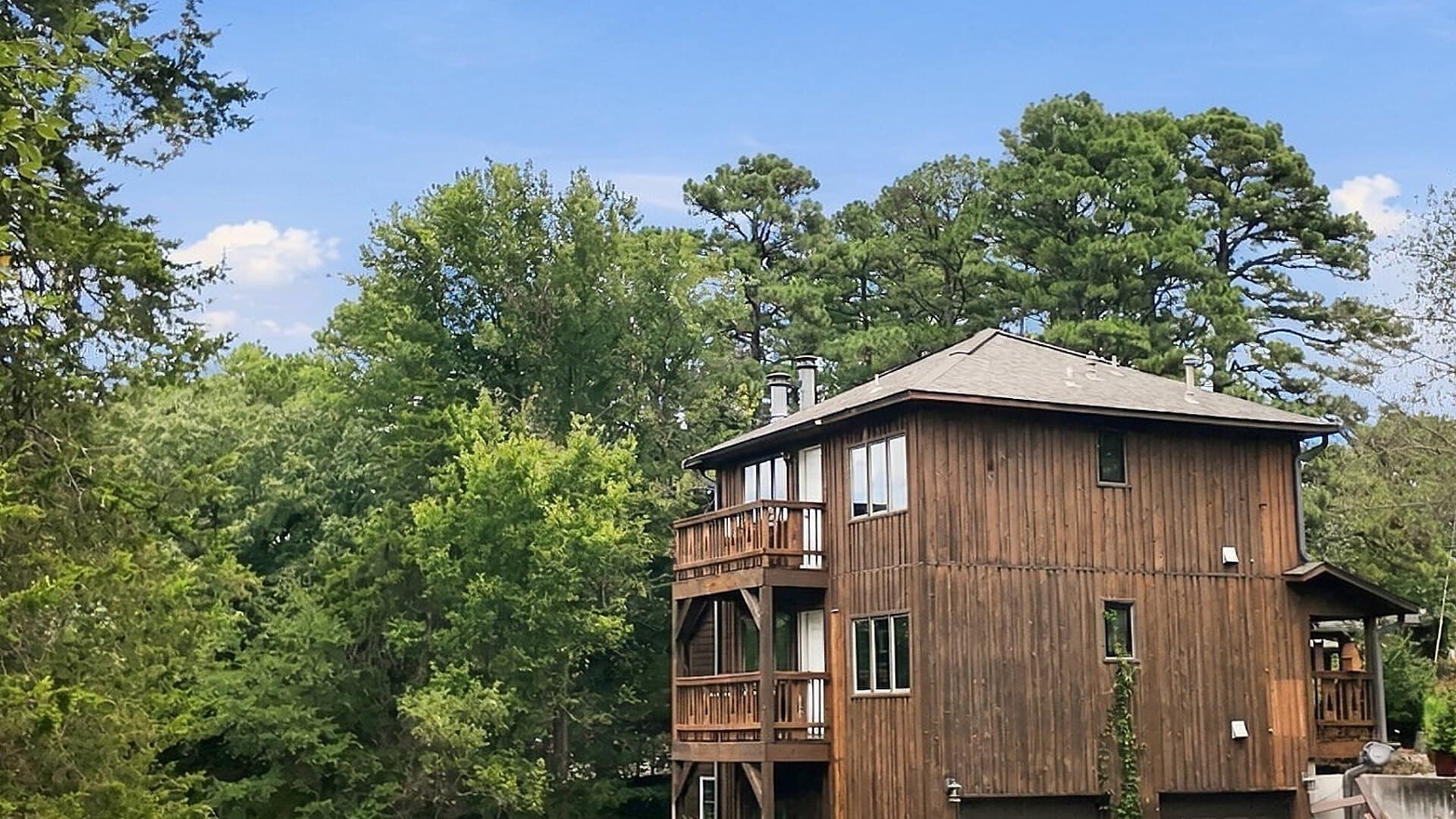 Wooden house surrounded by lush trees under a clear blue sky.