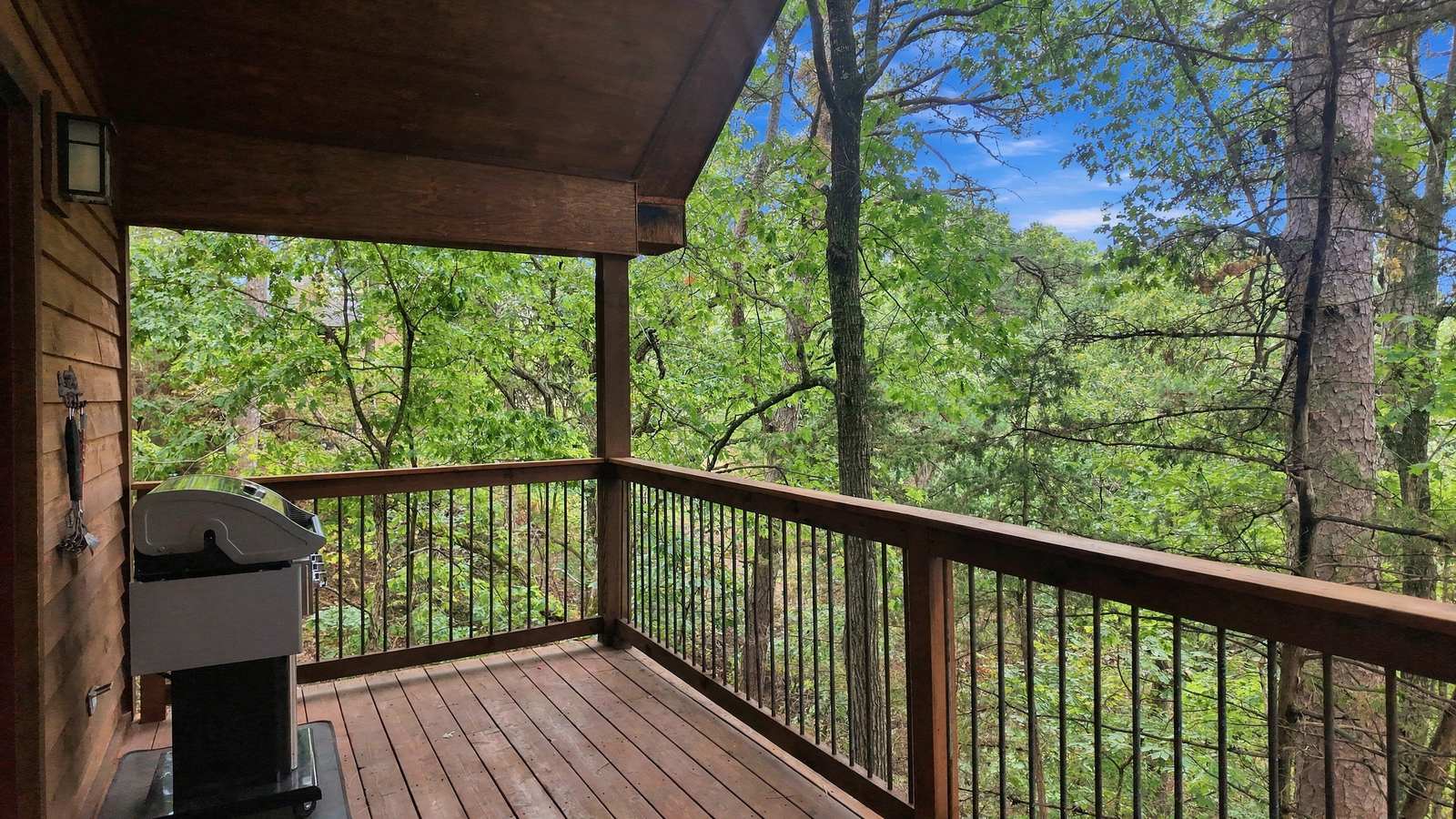 A wooden deck surrounded by lush green trees and a grill.