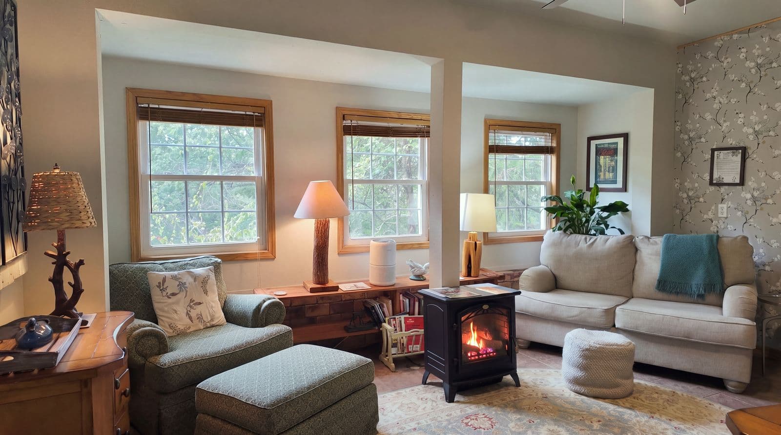 Cozy living room featuring a green armchair, a white sofa, and a fireplace surrounded by natural light from multiple windows.