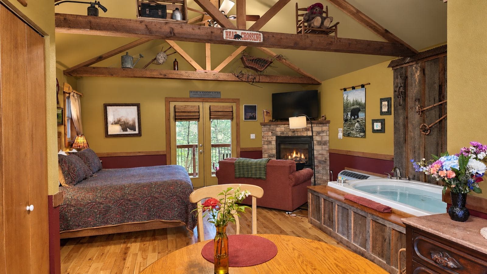 Cozy cabin interior featuring a bed, fireplace, seating area, and a hot tub, with wooden accents and warm lighting.