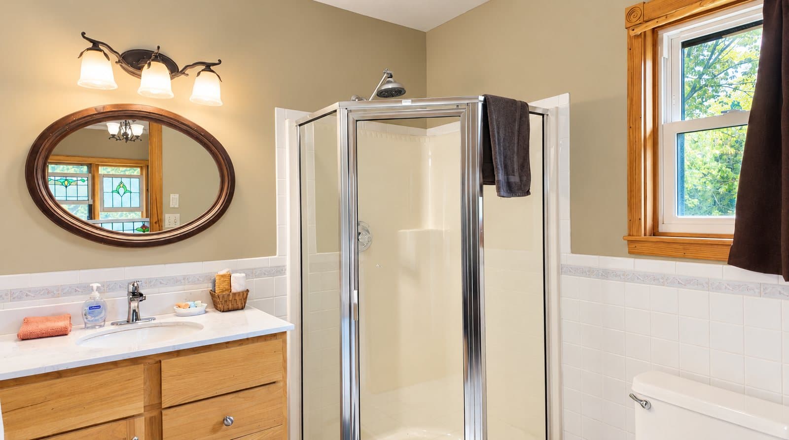 A bright, modern bathroom featuring a glass shower, wooden vanity, and a round mirror.