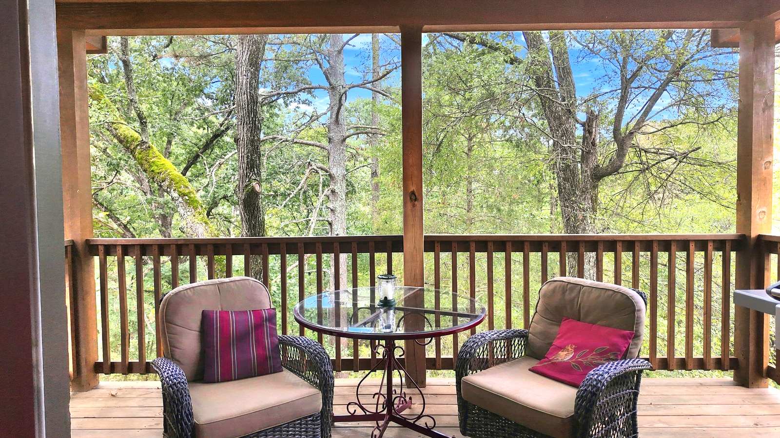 A cozy porch with two armchairs and a glass table, surrounded by greenery and trees.