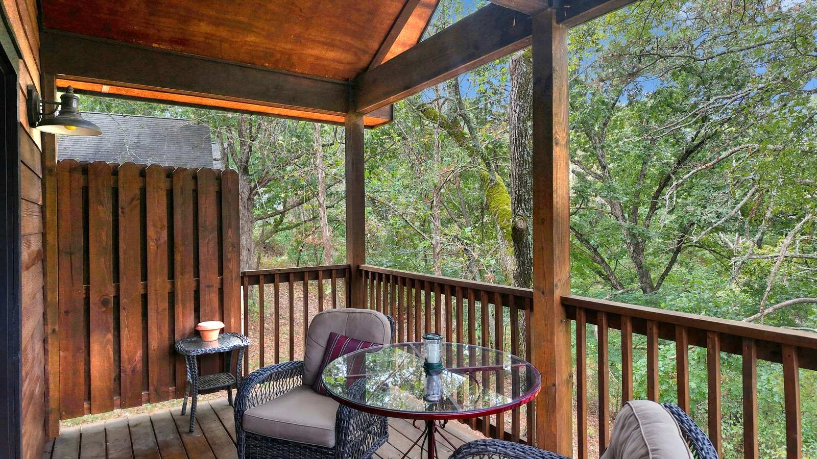 A cozy wooden porch with two chairs and a small glass table surrounded by greenery.