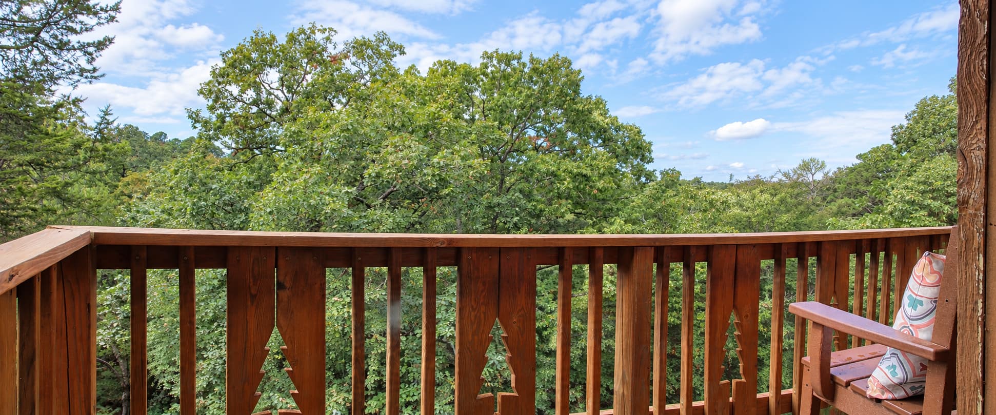 Wooden balcony overlooking a lush green landscape under a blue sky.