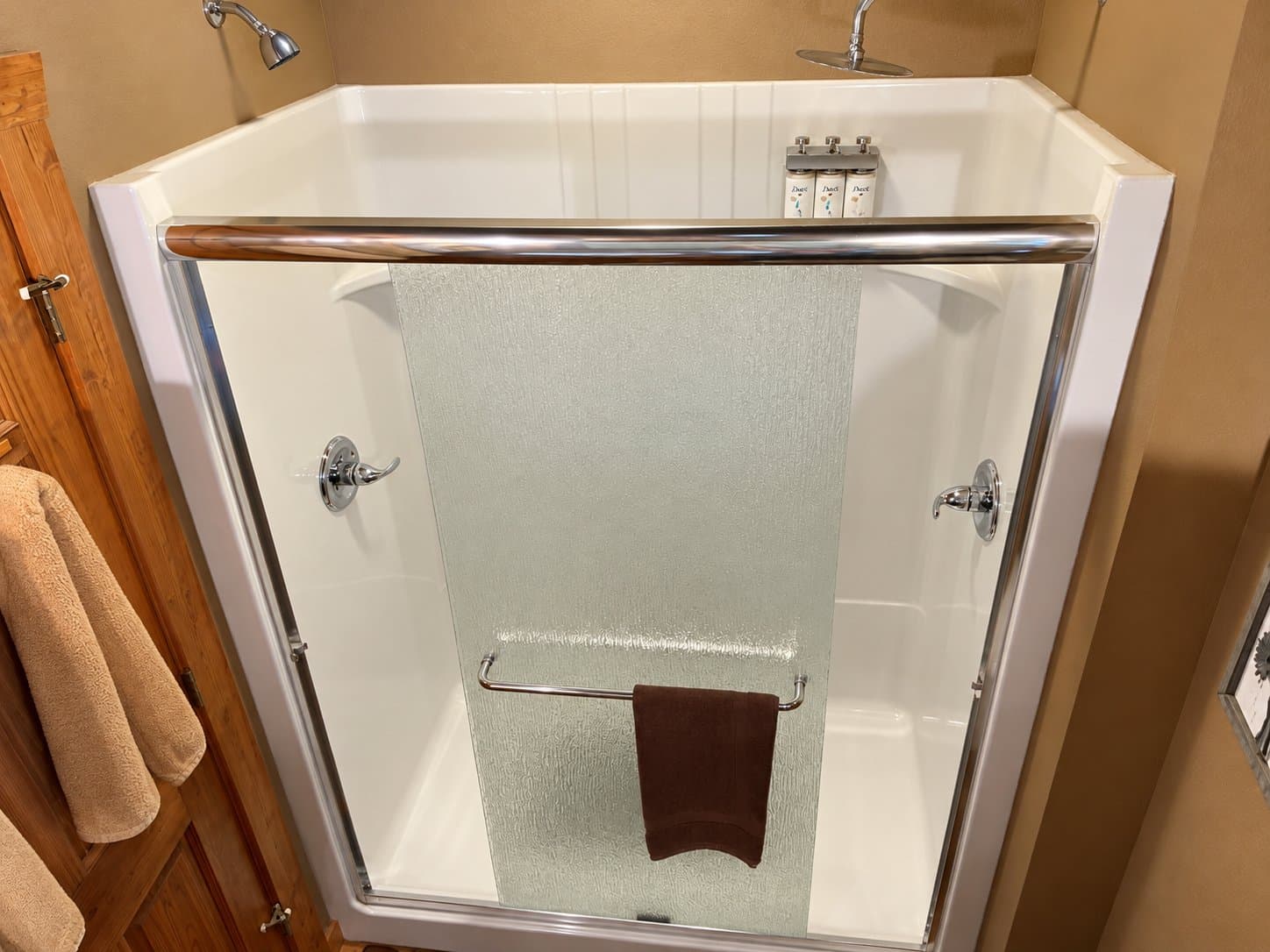 A corner shower with a glass door, chrome fixtures, and a towel hanging on a bar.