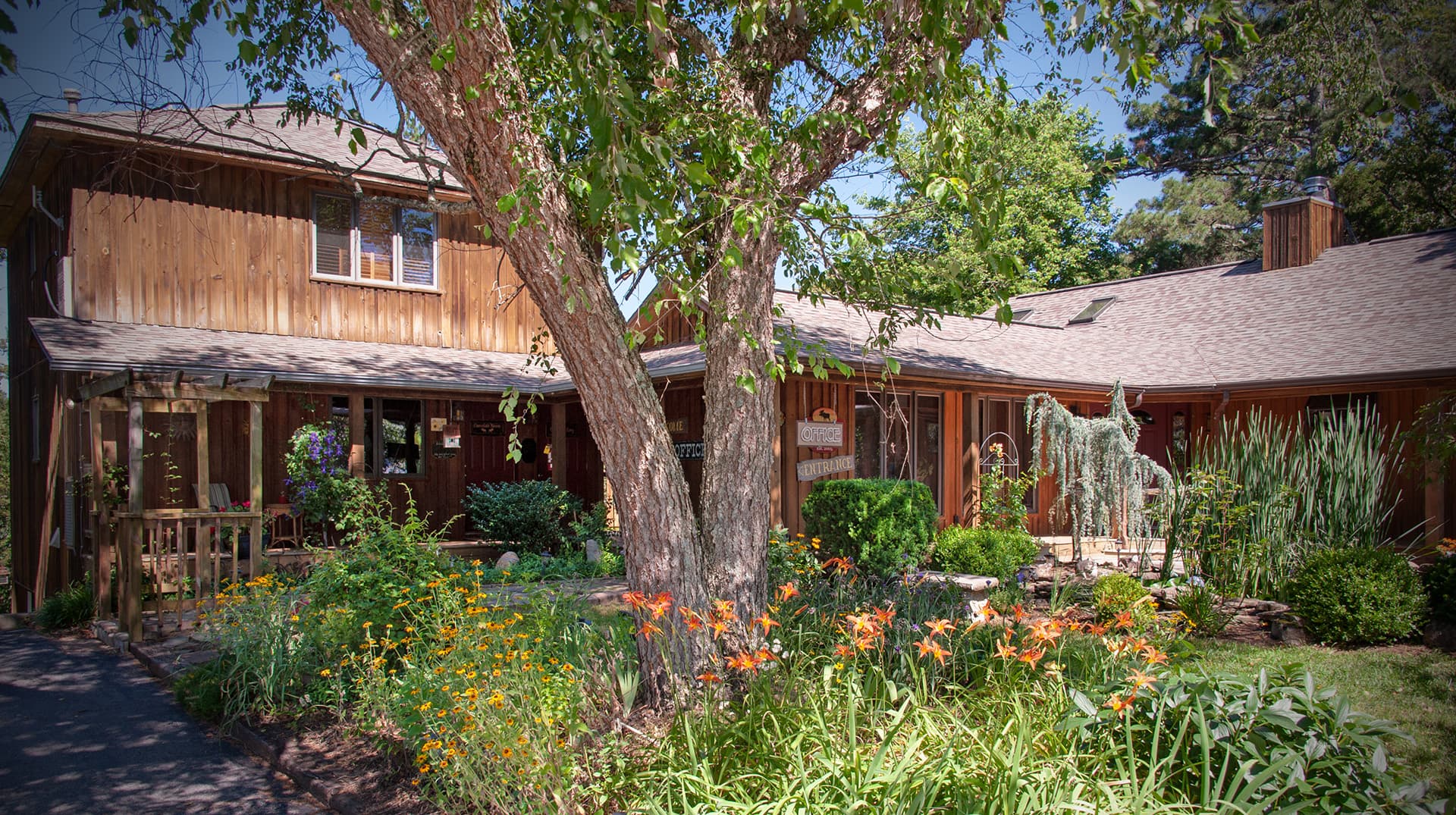 A warm, wooden-paneled home surrounded by lush greenery and vibrant flowers.