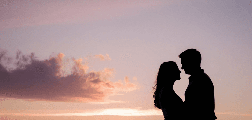 A silhouetted couple embraces against a colorful sunset sky. A silhouetted couple embraces against a colorful sunset sky.